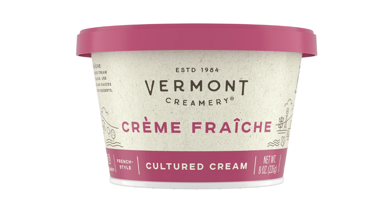 A tub of Vermont Creamery Crème Fraïche cultured cream, featuring a textured off-white label with pink and dark red accents and a matching pink lid, set against a plain white background.