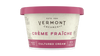 A tub of Vermont Creamery Crème Fraïche cultured cream, featuring a textured off-white label with pink and dark red accents and a matching pink lid, set against a plain white background.