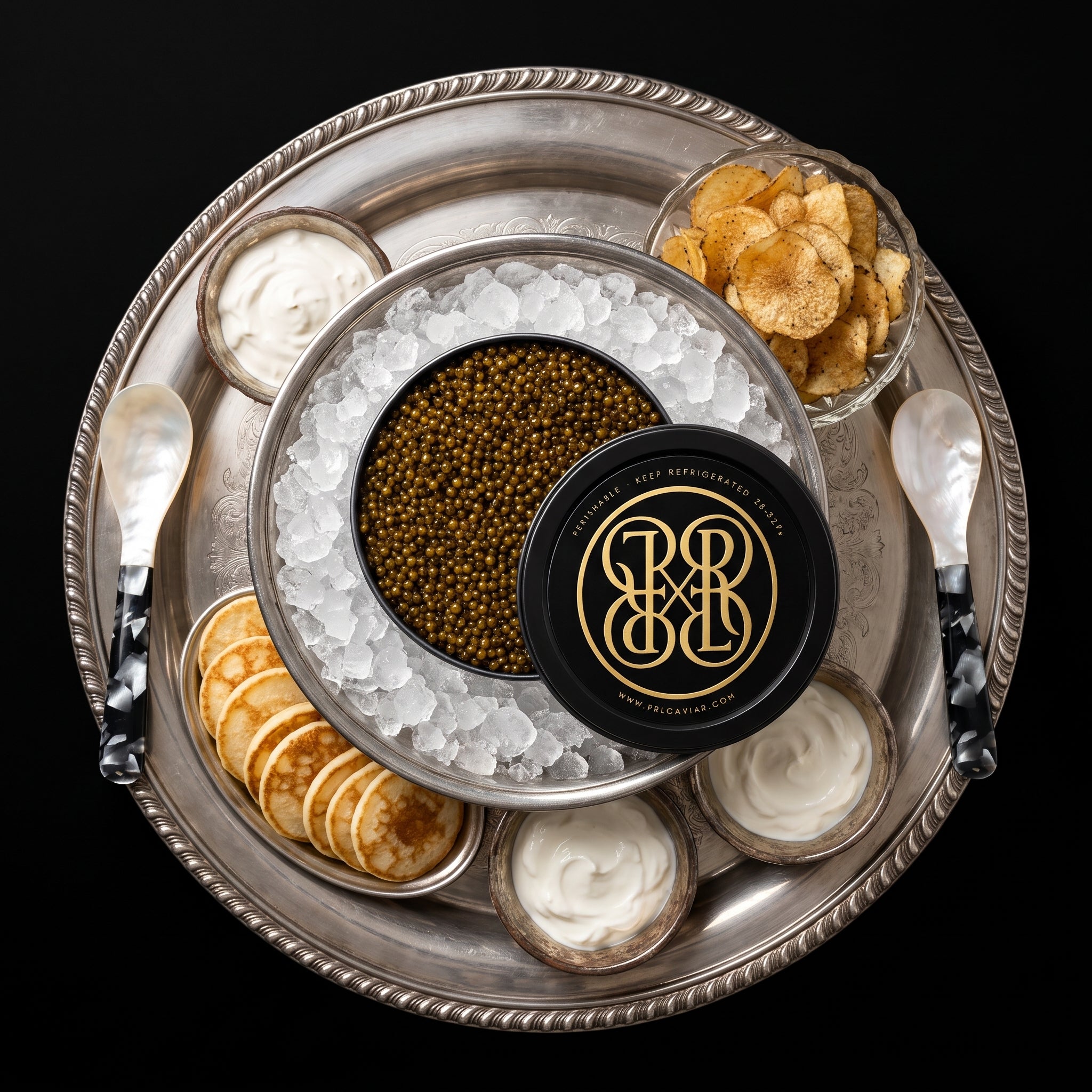 The Party Kit: a large PRL caviar tin on ice on a silver platter with party spoons, mini blinis, black truffle potato chips and crème fraîche
