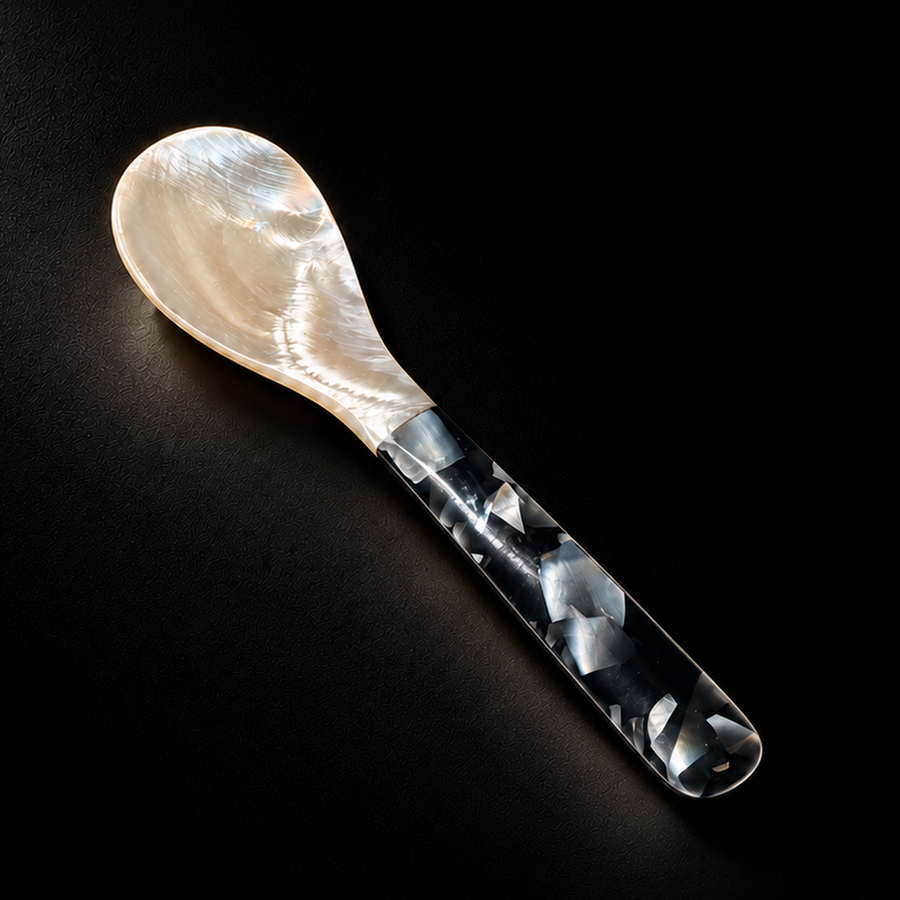 A decorative spoon with a pearlescent cream-colored bowl and a marbled black, white, and gray handle, photographed on a dark black background.